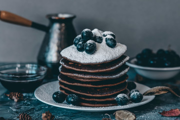 Pancakes on a white plate in powdered sugar with grapes on a gray background.