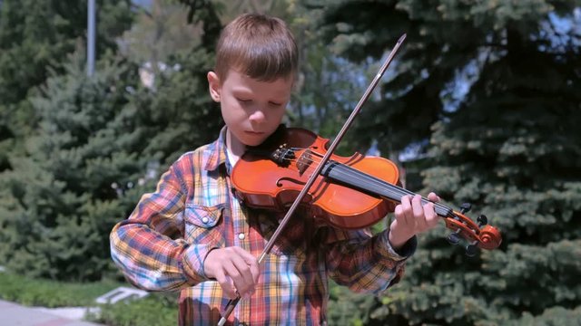Child boy is playing the violin standing in park in the city. Portrait of little musician. Education learn play violin boy teen violinist instrumentalist performance melody.