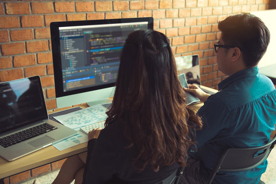 Two software developers are using computers to work together with their partner at the office desk.