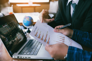 young business man hand holding pen and pointing graph chart discussing with colleagues about...
