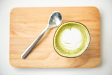 Hot green tea latte with spoon on wooden plate