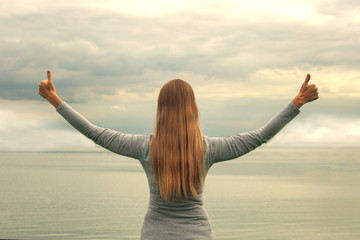 A beautiful girl stands on the shore with her back to the camera. Hands up. Sunset. Yoga classes.