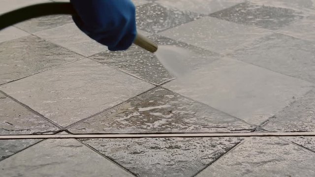 Hand of man wearing blue rubber gloves using a hose to cleaning the tile floor.
