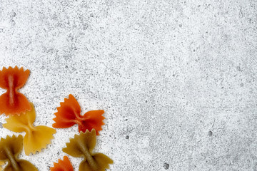 Types of uncooked pasta. Green, yellow and red pasta farfalle dry on a light concrete background. Shooting from above. Flat lay, top view, copy space.