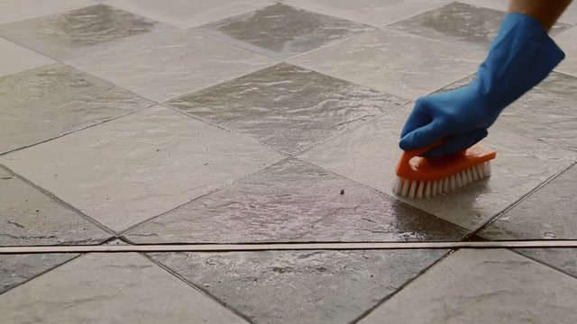 Hand of man wearing blue rubber gloves is used to convert scrub cleaning on the tile floor.