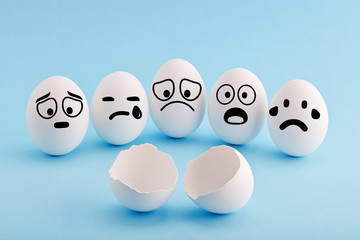 White chicken eggs with faces gathered around a broken egg shell and mourning with sad and shocked...