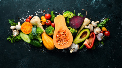 Fresh seasonal vegetables on a black stone background: Pumpkin, tomato, avocado, cucumber, onion,...