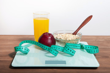 The concept of healthy diet, fitness and weight loss. Scales, measure tape, oatmeal, apple, a glass of juice on the table.