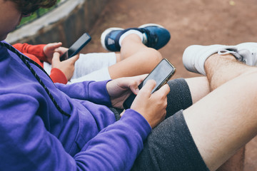 Close up view of a couple of teen using smartphone sitting outdoor at the park. Teenagers communicate with new technology devices with remote friends. Youth, new tech trend and communication concept.