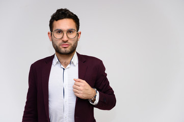 Men's fashion concept. Portrait of a handsome male model in glasses shows hands wearing a dark jacket, posing on a gray background. Black hair. Close Studio Shot