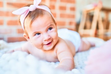 Adorable baby lying down over blanket on the floor smiling happy at home. Newborn with smile on face relaxing and resting comfortable