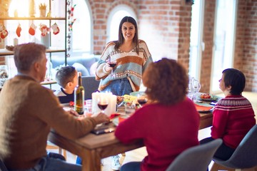 Beautiful family smiling happy and confident. One of them standing holding cup of wine speaking speech celebrating christmas at home