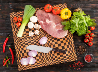 Meat, fresh vegetables and a knife on a cutting board