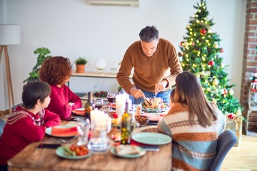 Beautiful family smiling happy and confident. One of them curving roasted turkey celebrating christmas at home