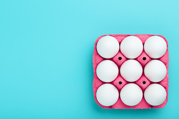 White chicken eggs in a pink carton tray box on blue background with copy space