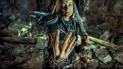 Post-apocalyptic woman with the chain and sword in hands on the dungeon background. Focus point on the arm with the rusty chain.