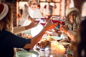 Beautiful group of women smiling happy and confident. Eating roasted turkey and toasting with cup of wine celebrating christmas at home