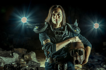 Post-apocalyptic woman with the rusty helmet in hands on the dungeon background. Nuclear post-apocalypse time. Life after doomsday