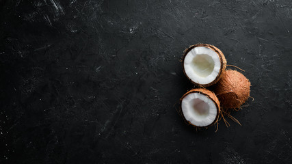 Coconut with palm leaves on a black stone background. Tropical Fruits. Nut. Top view. Free space...