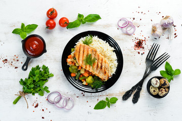 Baked chicken fillet with rice and vegetables on a black plate. Top view. Free copy space.