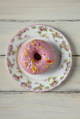 Donut with pink icing and sprinkles on a white wooden table