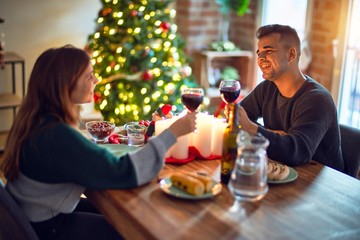 Young beautiful couple smiling happy and confident. Eating and toasting with cup of wine celebrating christmas at home