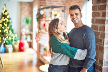 Young beautiful couple smiling happy and confident. Standing and hugging around christmas tree at home