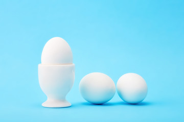 One white egg in an egg cup with two eggs on the floor
