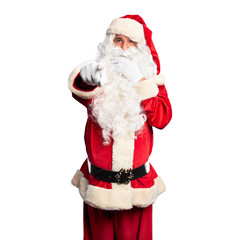 Middle age handsome man wearing Santa Claus costume and beard standing laughing at you, pointing finger to the camera with hand over mouth, shame expression
