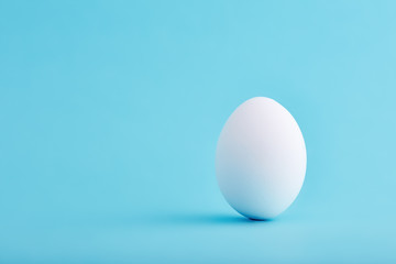 One white egg standing vertical on blue background