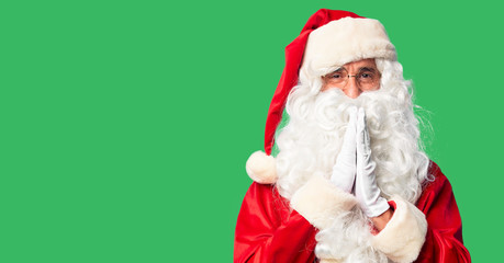 Middle age handsome man wearing Santa Claus costume and beard standing praying with hands together asking for forgiveness smiling confident.