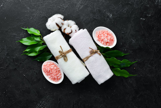 Pink sea salt with towels and tropical leaf. On a black stone background. Spa treatments. Top view. Free space for your text.