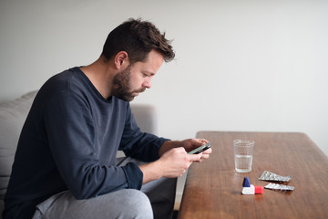 Man looking at phone after taking medicine while sick