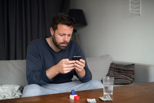 Man looking at phone after taking medicine while sick