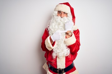 Middle age handsome man wearing Santa costume standing over isolated white background In hurry pointing to watch time, impatience, looking at the camera with relaxed expression