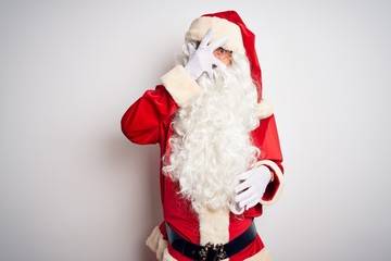 Middle age handsome man wearing Santa costume standing over isolated white background peeking in shock covering face and eyes with hand, looking through fingers with embarrassed expression.
