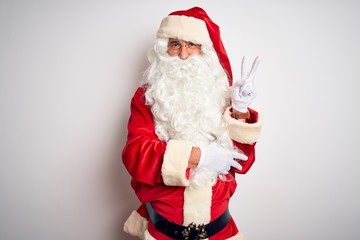Middle age handsome man wearing Santa costume standing over isolated white background smiling with happy face winking at the camera doing victory sign with fingers. Number two.