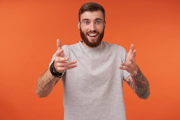 Happy lovely unshaved tattooed male with trendy haircut looking at camera cheerfully and raising...