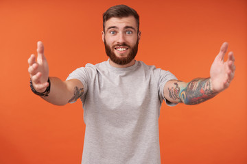 Studio shot of positive pretty young tattooed male with lush beard posing over orange background...