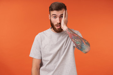 Exhausted bearded tattooed brunette male with short haircut looking tiredly to camera and keeping...