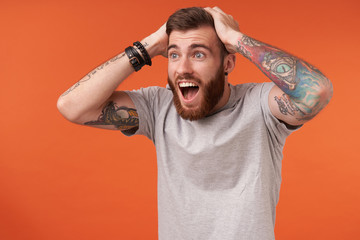 Overjoyed young unshaved tattooed brunette man wearing beige t-shirt and trendy accessories,...