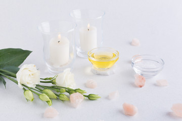 Spa composition with oils, sea salt, candles and a branch of white eustoma on a white background