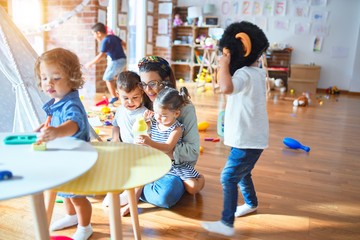 Beautiful teacher and group of toddlers playing around lots of toys at kindergarten