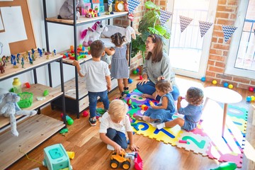 Beautiful teacher and group of toddlers playing around lots of toys at kindergarten