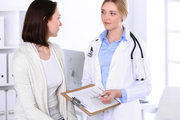Fototapeta premium Young woman doctor and patient at medical examination at hospital office. Blue color blouse of therapist looks good. Medicine and healthcare concept
