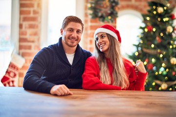 Young beautiful couple smiling happy and confident. Sitting on chair around christmas tree hugging at home