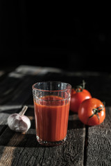 Glass of fresh tomato juice, tomatoes and garlic  on a dark   board