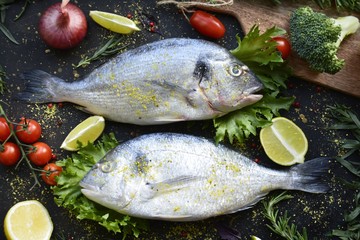 Fototapeta na wymiar fresh dorado fish with spices on a dark background, with lime, lemon, tomatoes and herbs flat lay