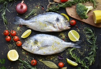 fresh dorado fish with spices on a dark background, with lime, lemon, tomatoes and herbs flat lay