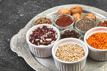 Beans and nuts selection in bowls: quinoa, chia, lentils, beans, almonds, walnuts, coffee beans on dark concrete background copy space